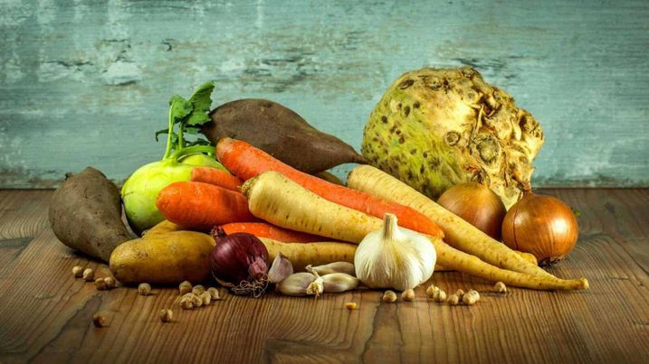 Verdure meglio cotte o crude. Quali più nutrienti? 2 Verdure crude o cotte: Pomodori, cipolle, aglio, carote, patate e pastinaca su tavolo di legno, collezione di verdure organiche fresche e salutari.