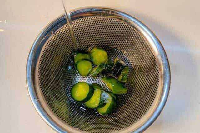 Cetrioli freschi immersi in acqua freda in un colino in acciaio, pronti per essere sciacquati o preparati per insalate e ricette healthy.
