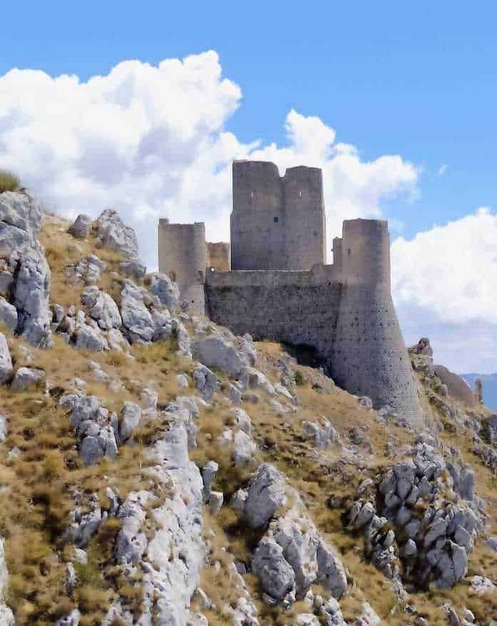 Castello medievale su una collina rocciosa, scenario storico e paesaggistico suggestivo, immerso in un paesaggio naturale ondulato con rocce e vegetazione secca sotto un cielo azzurro con nuvole.