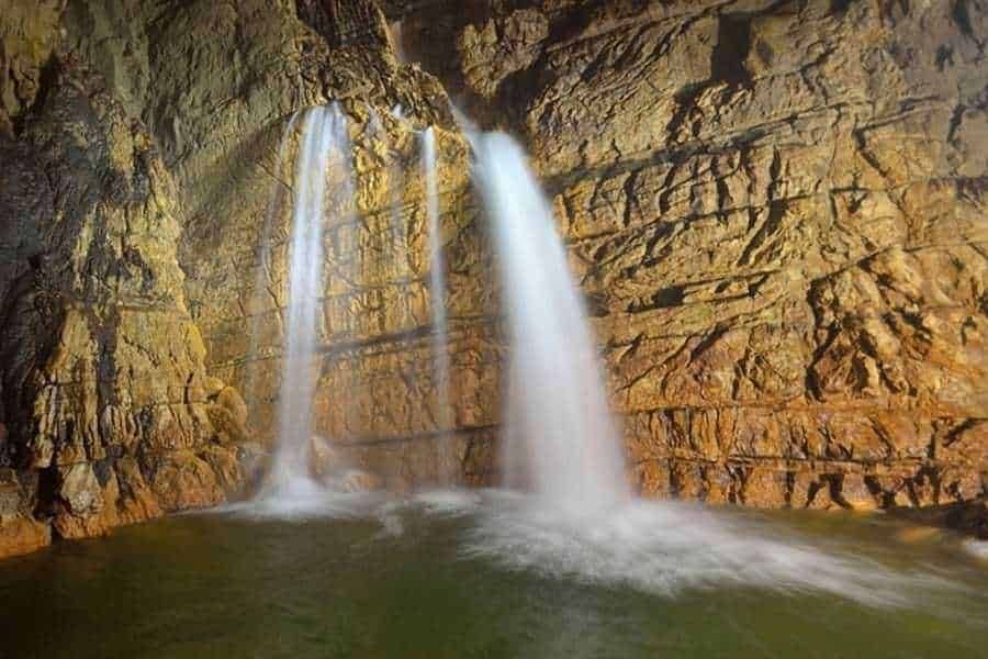 Acqua in cascata su scogliera rossa naturale, paesaggio di natura selvaggia, cascate spettacolari in isolata area naturale, ambiente naturale incontaminato, bellezza paesaggistica in montagna e acqua pulita.
