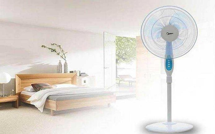 Il condizionatore fa male alla salute in estate? 5 Ventilatore a piantana in una camera da letto moderna con arredi minimalisti, illuminata dalla luce naturale, ideale per rinfrescare gli ambienti domestici durante le stagioni calde.