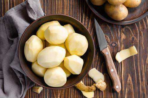 Patate pelate e pronte da cucinare in una ciotola di ceramica, con coltello su tavolo in legno, pronta per essere utilizzate in ricette di cucina tradizionale.