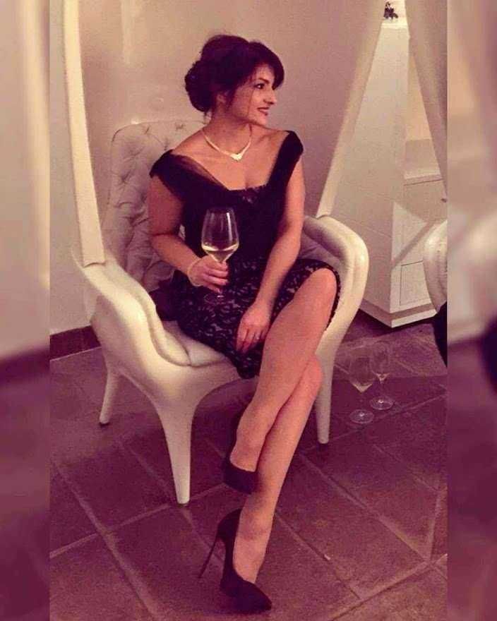 12 Tipi di tacchi scarpe iconiche 8 Elegante donna in abito nero con calze a rete e tacchi a spillo, seduta su una poltrona con calice di vino, atmosfera raffinata e glamour.