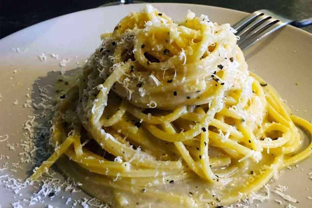 Spaghetti alla Carbonara con uova, pancetta e formaggio, serviti con una generosa spolverata di pepe nero e pepe nero macinato fresco, un piatto classico della cucina italiana.
