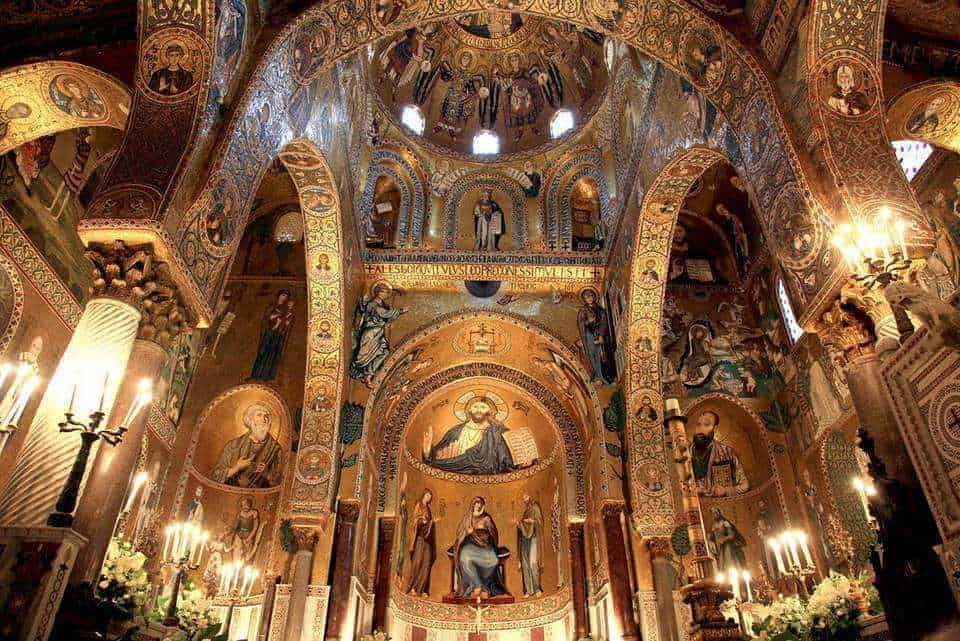 Mahé d'église ortodossa italiana decorata con mosaici dorati di icone religiose, archi elaborati e candelabri, rappresentando un importante esempio di arte cristiana orientale e patrimonio spirituale.