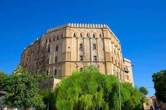 Antico castello Medievale con mura imponenti e torri, circondato da alberi verdi e cielo azzurro, sito storico in Italia, esempio di architettura e cultura medievale.