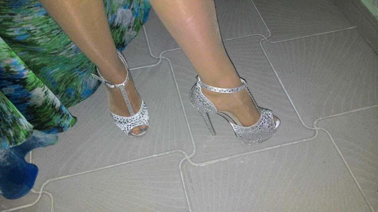 Sandali eleganti con tacco alto in argento e dettagli in pandant, abbinati a un vestito colorato, su pavimento in piastrelle, stile sofisticato e glamour.