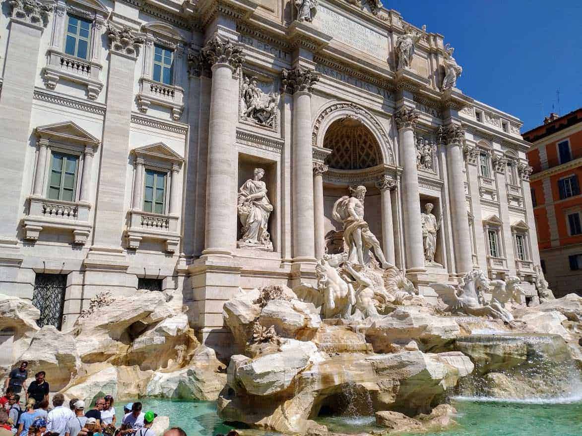 Fountain of the Trevi in Rome with intricate baroque sculptures, grand architecture, and flowing water, attracting many visitors to this iconic Italian landmark.