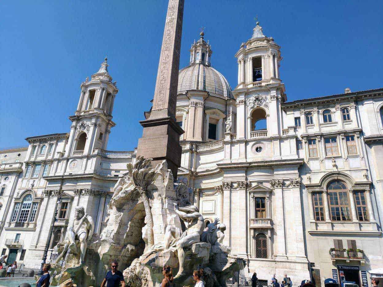 Fili ALT: Fontana delle Quattro Fiumi di Bernini a Piazza Navona, Roma, monumento storico barocco con sculture dettagliate sotto un cielo azzurro.