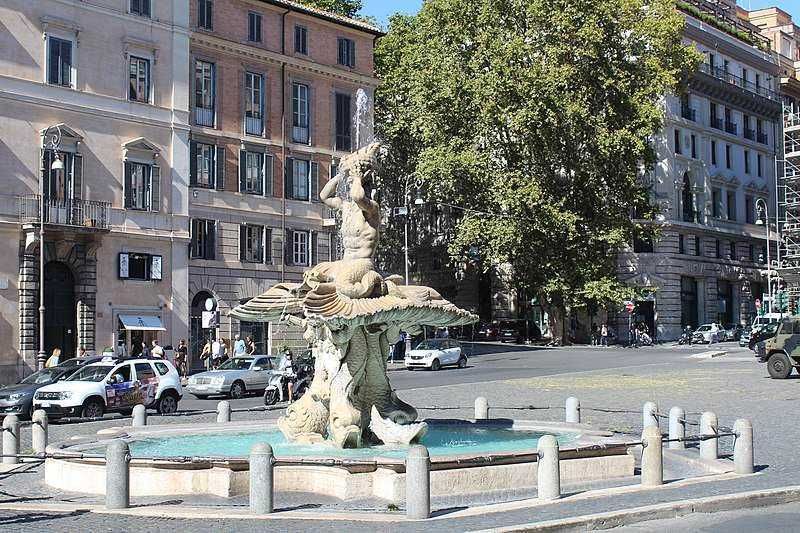 13 Fontane storiche di Roma celebrative 10 Elegante fontana storica in piazza con edifici antichi e strade trafficate, simbolo di Roma. La fontana decorativa con statua di pietra si trova al centro di un vivace quartiere urbano.