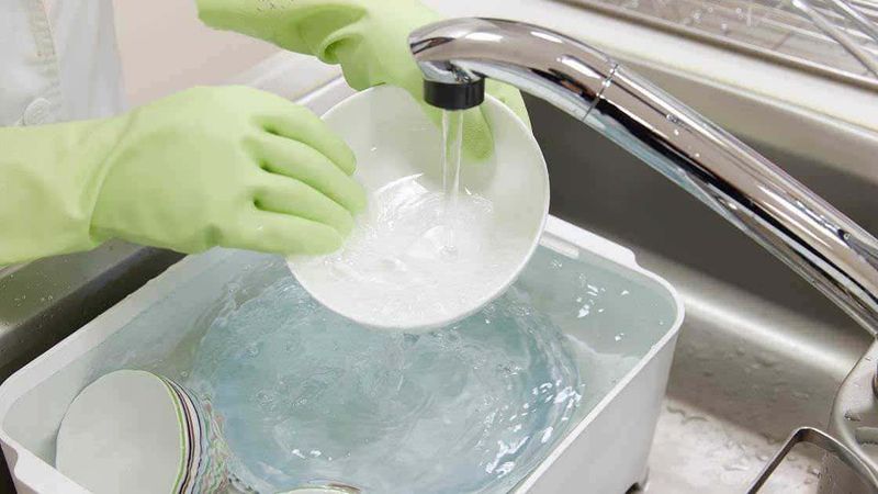 Candeggina dove non usarla, 12 errori 3 Lavaggio di piatti con guanti di gomma, lavatrice e acqua pulita, immagine di pulizia della cucina, igiene e sanificazione, cura degli utensili da cucina.