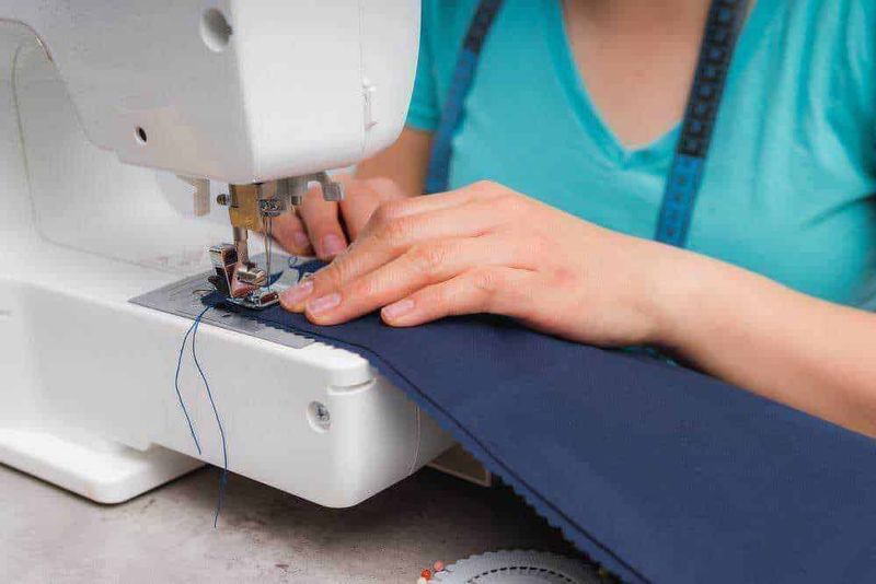 Come scegliere una macchina da cucire per principianti 3 Sewing machine stitching navy blue fabric, detailed view of hands and sewing process, professional textile craftsmanship, tailor work, fashion design, creative sewing project, craftsmanship.