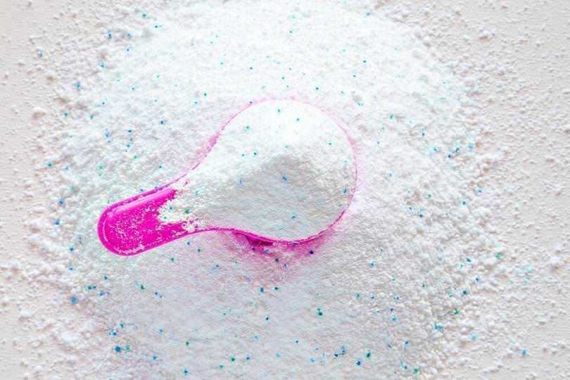 Polvere bianca in polvere con cucchiaino rosa, evidenziando ingredienti per cucina o prodotti di bellezza, su sfondo neutro.