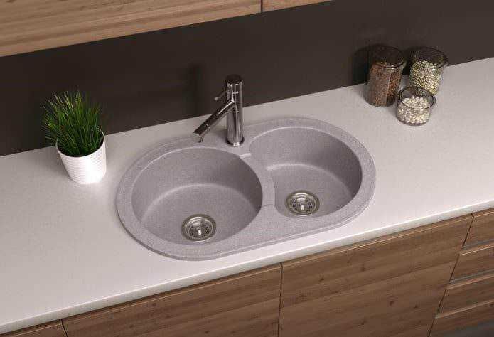Lavello a incasso o da appoggio: Lavello da cucina con due fosse in acciaio inox, piano di lavoro in superficie bianca e ante in legno chiaro, decorato con piantina e barattoli di spezie.