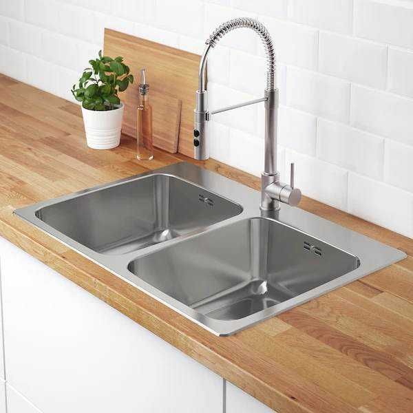 Lavello in acciaio inox doppio con rubinetto moderno in una cucina con piani di lavoro in legno e pareti bianche.