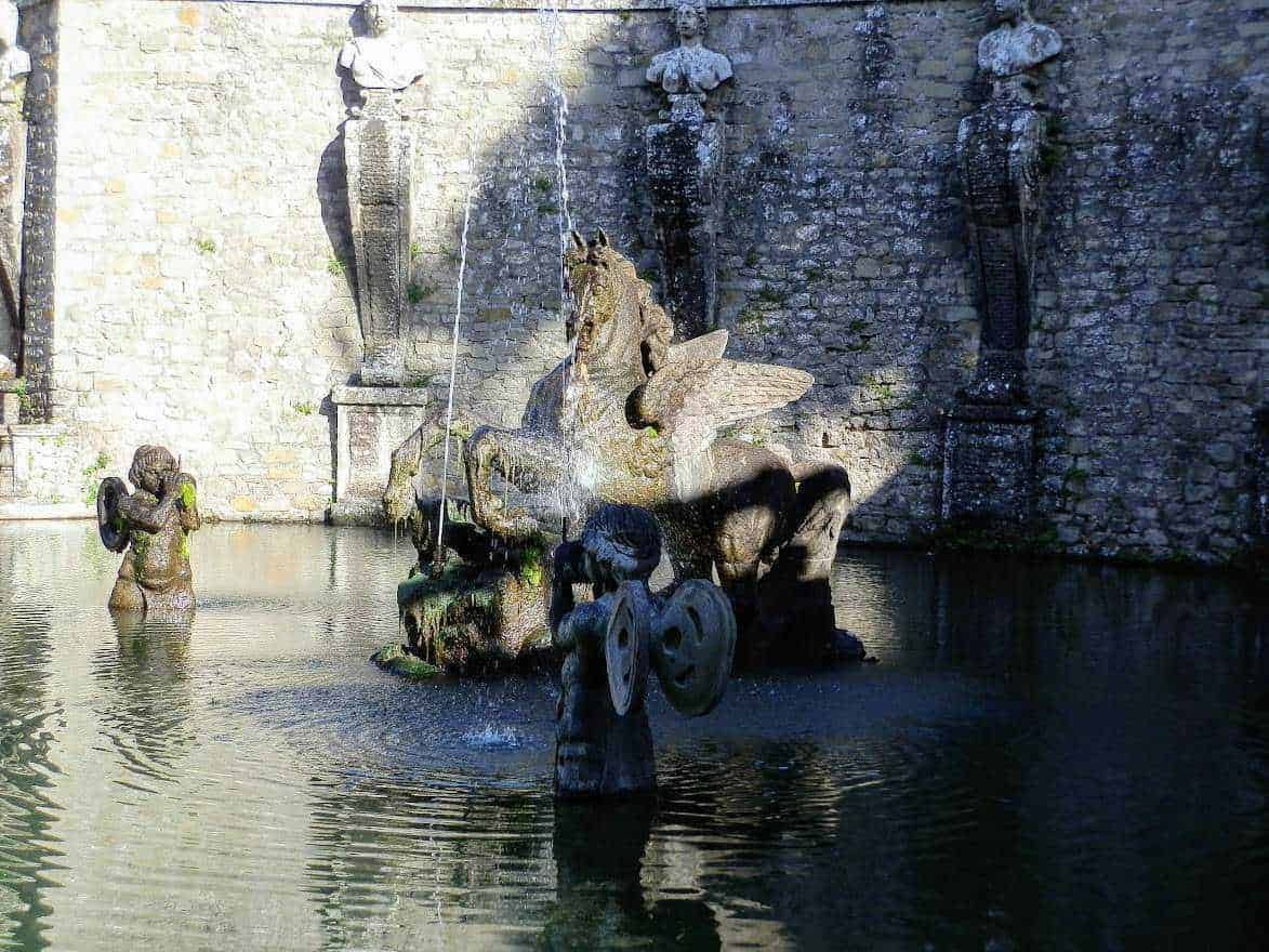 Fontana artistica con cavallo mitologico e maschere in pietra, fontana storica nel centro di un cortile antico. Scultura in pietra, sui toni del grigio e verde, immersa in acque tranquille.