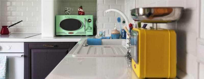 Microonde verde sulla mensola della cucina con altri elettrodomestici e utensili da cucina.