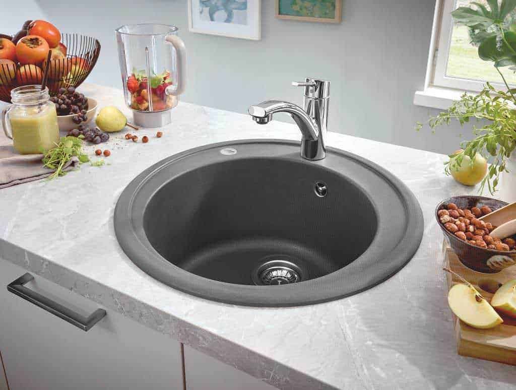 Miglior materiale per il lavello da cucina: Lavandino da cucina nero con rubinetto in acciaio inossidabile, superficie in marmo chiaro, con frutta fresca e utensili, ideale per ambienti moderni e funzionali.