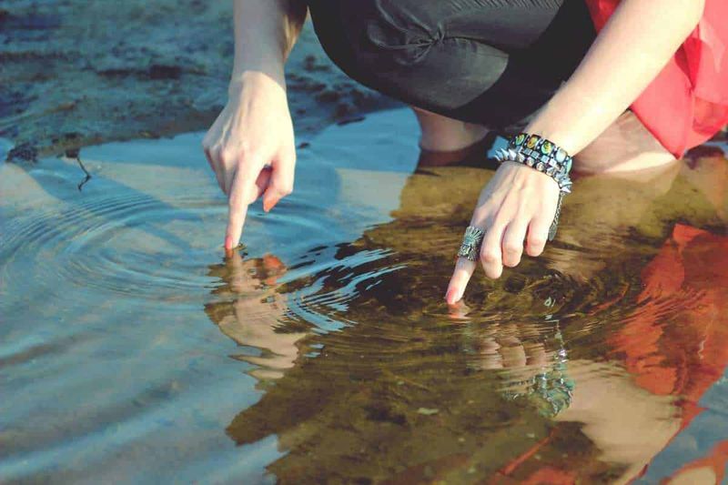 Quante perle nel bracciale, pari o dispari? 3 Titolare Web. Foto di una persona che rovista nell'acqua di un ruscello con le dita. Scarpe da ginnastica e accessori decorative alla mano, ambiente naturale. Ideale per immagini di natura, avventura, esplorazione e outdoor.