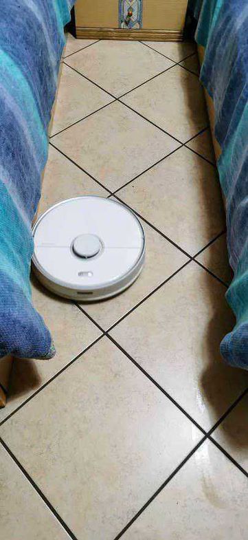 Robot Roborock S5 Max aspira e pulisce ogni ambiente 8 Pulitore robot aspirapolvere intelligente per la casa, scorre tra i mobili su un pavimento di piastrelle.