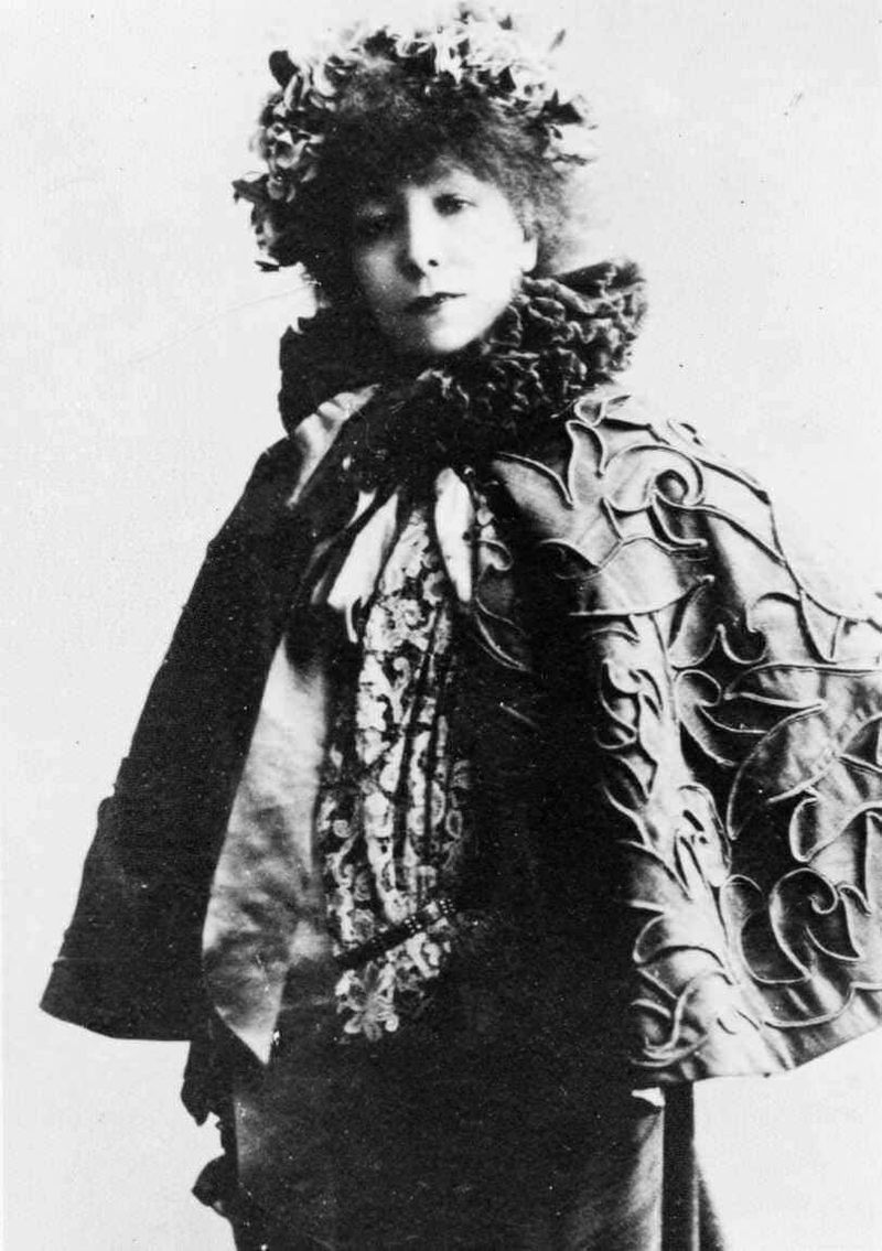 Storia del rossetto rosso nel tempo 4 Elegante ritratto in bianco e nero di una donna con abiti storici, cappello con fiori e mantello riccamente decorato, stile vintage, repertorio di moda d'epoca.