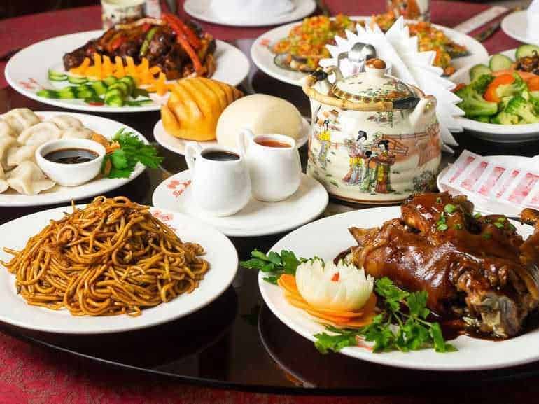 Finestra di piatti di cucina cinese tradizionale con noodles, involtini, salsa, carne, verdure e teiere decorative, ideale per apprezzare i sapori autentici dell'Oriente.