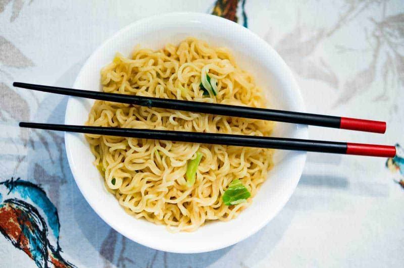 Cultura e tradizioni della Cina, 12 usanze interessanti 4 Deliziosi noodles istantanei in una ciotola bianca con bacchette nere e rosse, pronti per essere gustati, rappresentano la cultura culinaria asiatica.