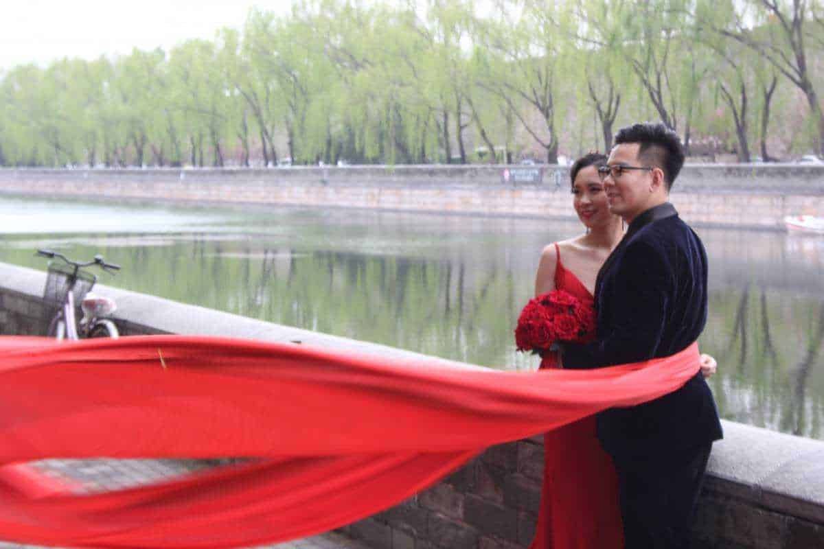 Bacio tra coppia di sposi con velo rosso lungo sul fiume in città, vista romantica e celebration matrimoni, fotografia di coppia felice, emozioni e amore, eventi speciali all'aperto.
