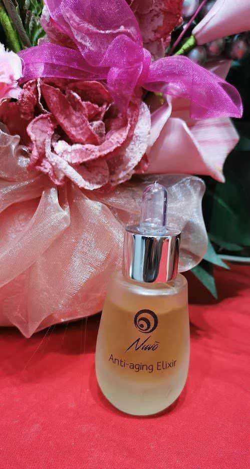 Siero alla bava di lumaca: Anti-aging Elixir siero viso sotto forma di bottiglia con pipetta, in primo piano su sfondo floreale rosa e tessuto shabby chic, ideale per la cura della pelle e ringiovanimento facciale.