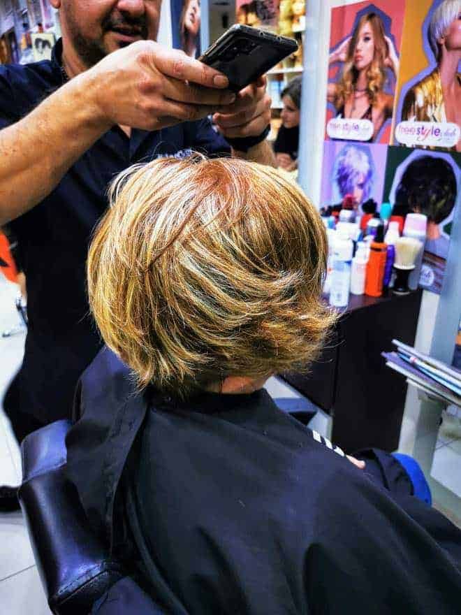 Lunga immagine di una donna che riceve un taglio di capelli professionale presso un salone di bellezza, con prodotti per capelli e poster di acconciature sullo sfondo.