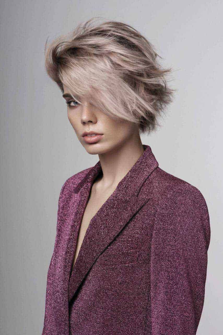 Aggiornamento stile capelli corti con frangia side-swept e texture breve, abbinato a giacca glitterata. Perfetto per look moderni e alla moda.