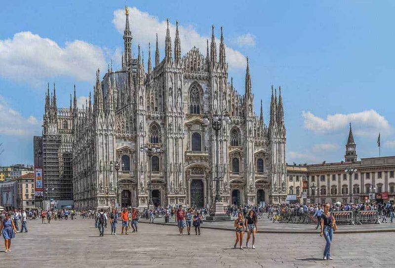 Arte medievale caratteristiche e sviluppo 7 Elegante immagine del Duomo di Milano con persone che passeggiano nella piazza, ideale per articoli su turismo, architettura e viaggi in Italia.