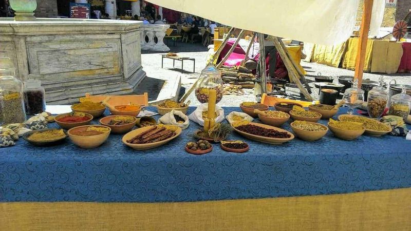 Cosa mangiavano nel medioevo i ceti sociali? 6 Pane di spezie e dolci tradizionali in esposizione a uno stand di mercato all'aperto. Vari dolci secchi, spezie e confetture presentati in ciotole di ceramica su un tavolo coperto da una tovaglia blu. Ambiente vivace, perfetto per appassionati di gastronomia locale e prodotti tipici.