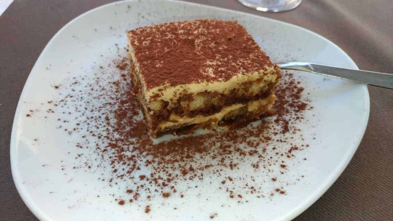 Tiramisu classico italiano con crema al mascarpone e cacao in polvere, servito su piatto bianco. Perfetto dolce tradizionale e dessert irresistibile per ogni occasione speciale.