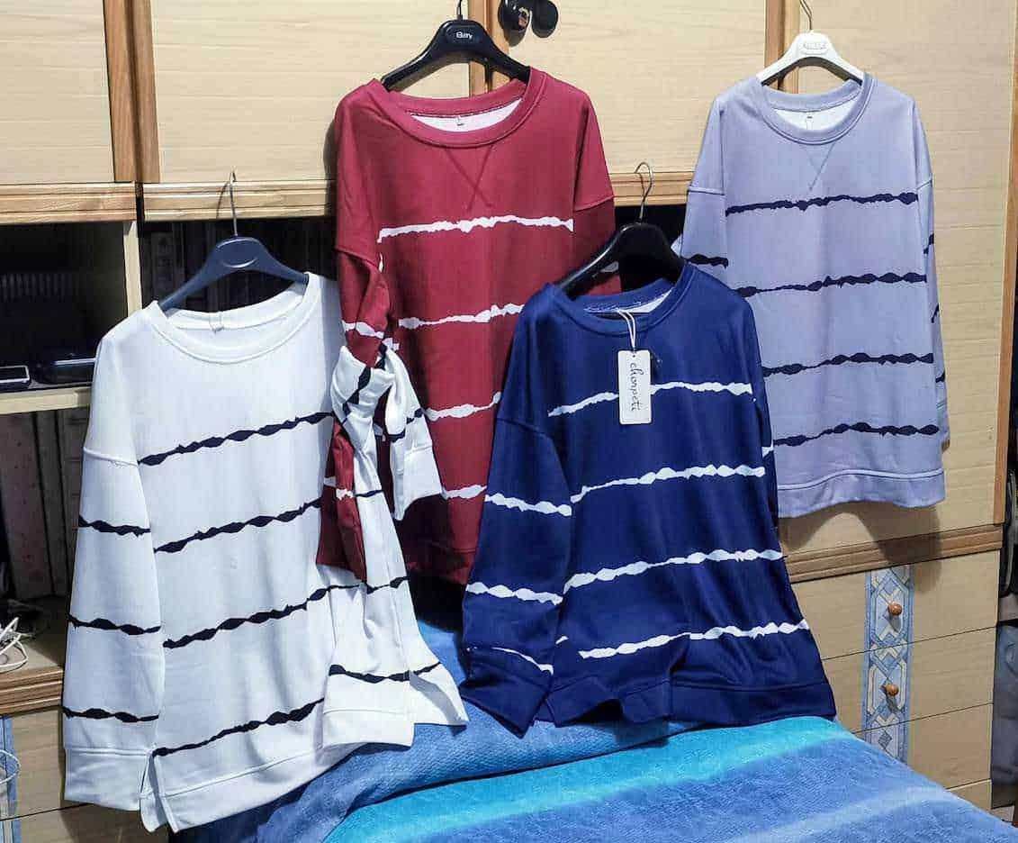 Magliette a righe colorate esposte su appendini in negozio di abbigliamento.