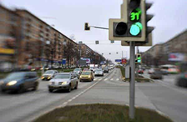Auto in movimento sotto semaforo verde in strada urbana congestionata, vista in notturna con traffic light e veicoli, immagine di traffico e viabilità in città, immagine di strada cittadina.