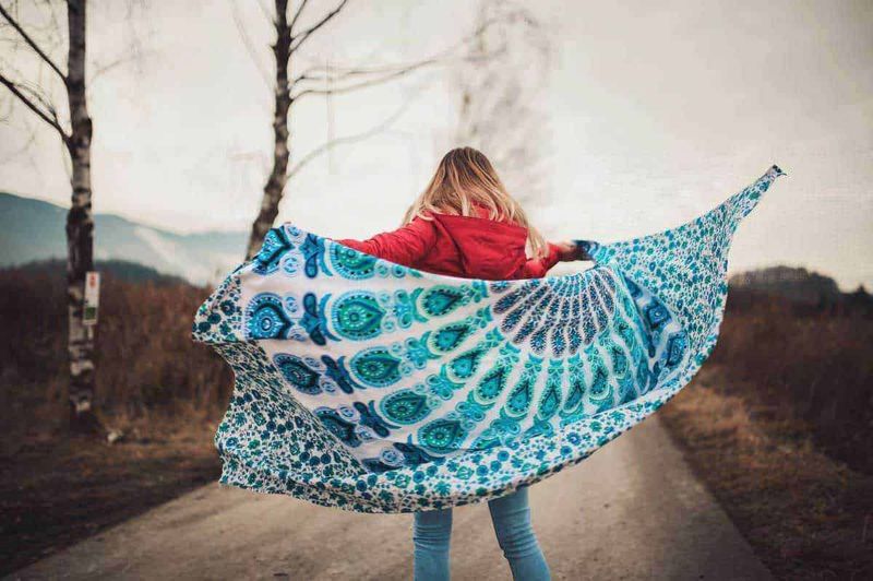 Storia dello scialle usi e design 6 Colorata sciarpa con motivi paisley blu e verde, indossata da una donna in una campagna autunnale, creando un effetto di movimento e libertà, ideale per immagini di moda, natura e stile di vita.