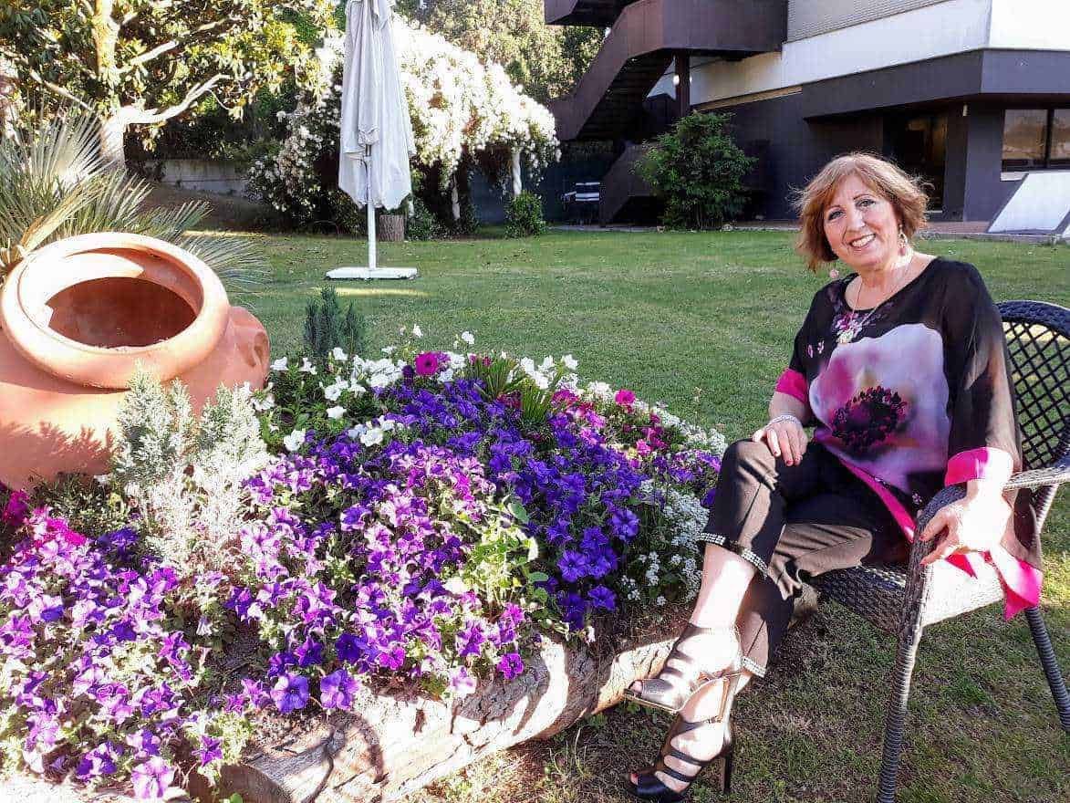 Fiori colorati e giardino rilassante con donna seduta su sedia di fronte a un grande vaso in terracotta, atmosfera estiva, benessere, natura, colore, relax, appunti sul blog.