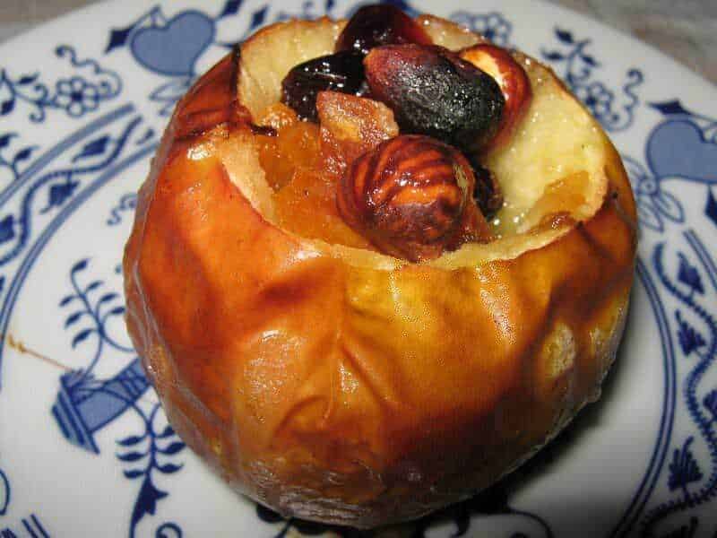 Mela cotta ripiena di frutta secca e miele, un dolce tradizionale italiano decorato con noci, mandorle e uvetta, servito su piatto di porcellana decorata blu e bianco.