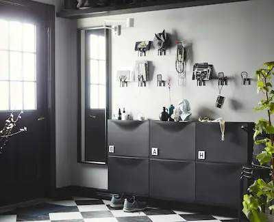 Stanza moderna con mobili eleganti, pareti decorate con oggetti e piante verdi, luce naturale da grandi finestre, atmosfera accogliente e di design.