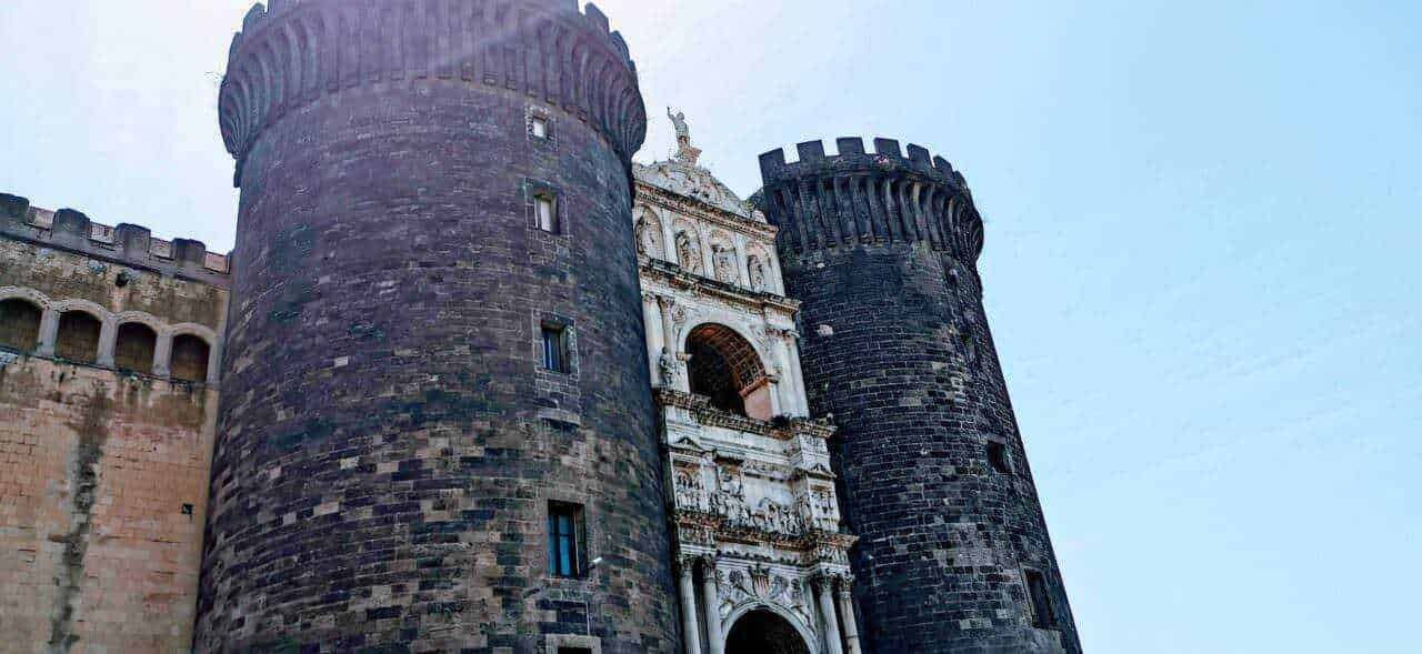 Antica fortezza con torri in pietra nera e ingresso barocco, situata in Italia, esempio di architettura storica e monumentale.