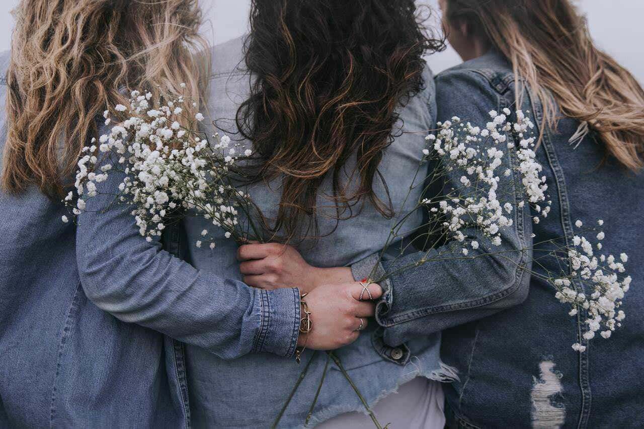 Fiore di gypsophila tra tre donne con denim, scatto ravvicinato durante il giorno, atmosfera spontanea e naturale, stile boho chic, simbolo di amicizia e moda casual.