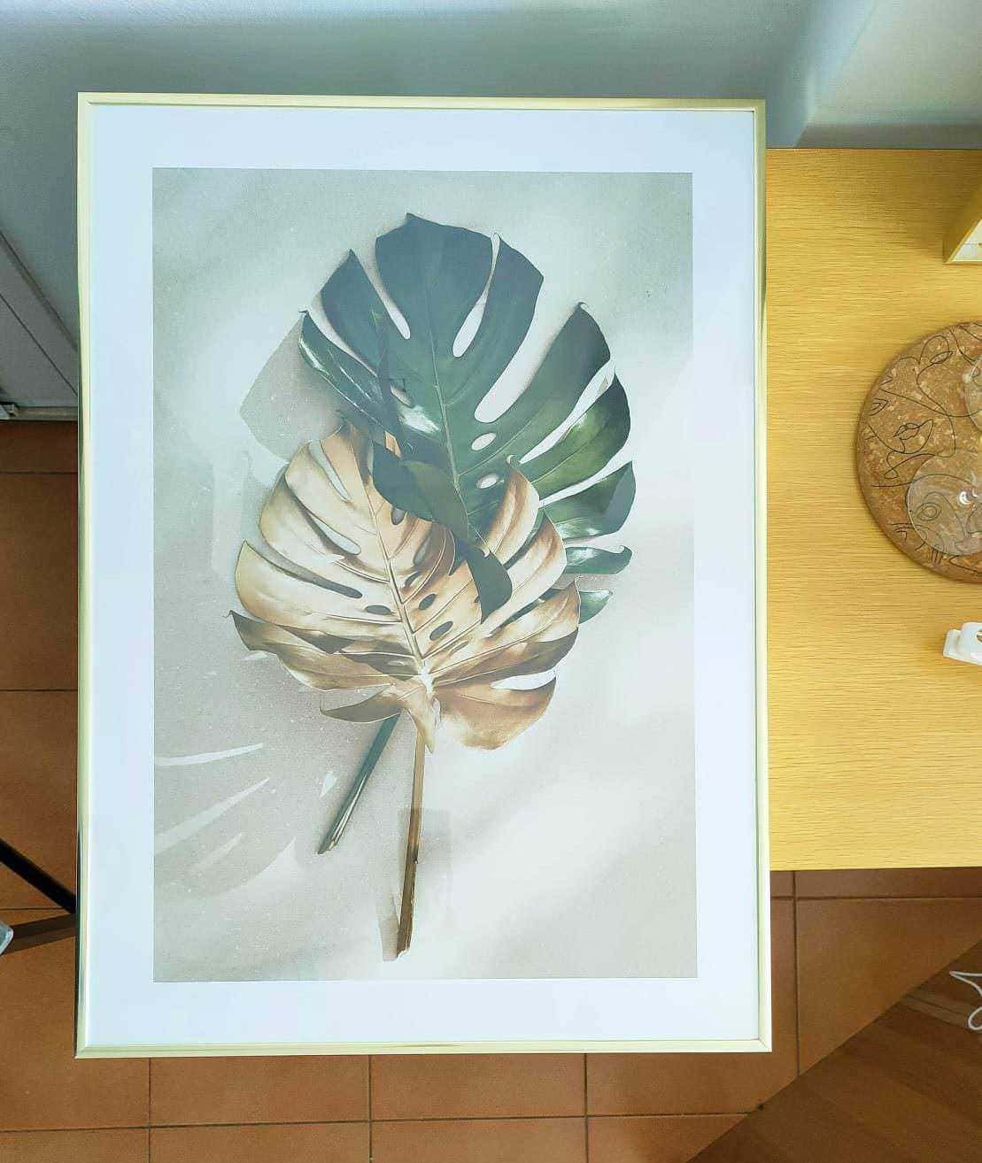 Foglia di monstera dipinta in stile artistico, decorazione moderna per interni, nei toni verdi e beige, quadro su tavolo in ambiente luminoso.