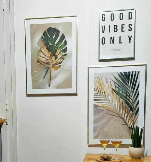 3 Poster foglie tropicali Golden Vibe in cucina 2 Tovagliette di foglie tropicali decorano una parete con quadri botanici e un poster con la scritta "Good Vibes Only", creando un ambiente accogliente e in stile naturale.