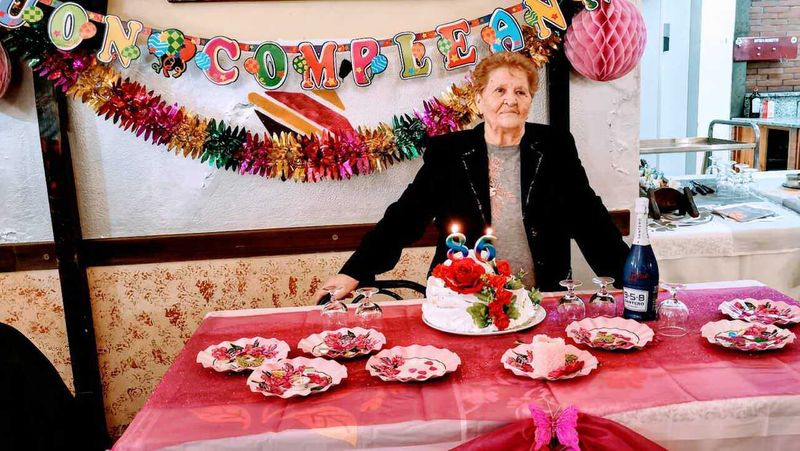 Come organizzare una festa di compleanno a sorpresa in 5 passi 2 FOTO: Anziana donna sorridente con torta di compleanno decorata con rose rosse, allegria e festa, decorazioni di compleanno colorate, brindisi con spumante, buon intrattenimento in famiglia.