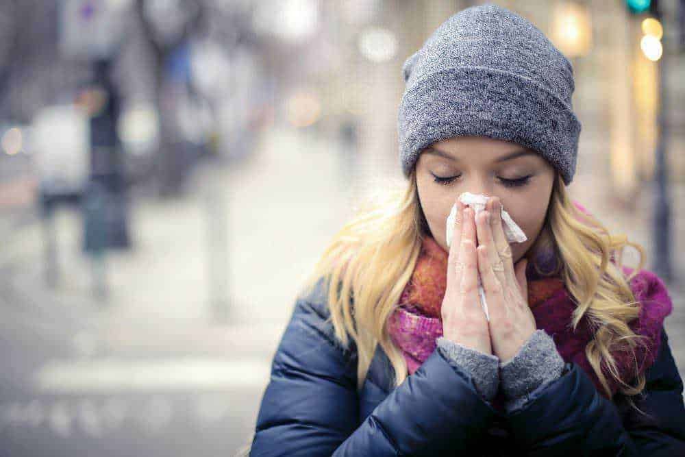 Naso di donna che si soffia il naso con fazzoletto in strada durante l'inverno, ambiente urbano freddo, malattia influenzale, donne con giacche e cappelli, influenza inverno.
