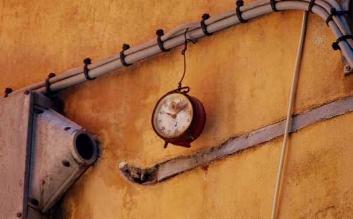 Vecchio orologio da parete appeso su una parete inmurata con tubature visibili e tubo di scarico, atmosfera vintage e urbana, dettaglio di arredamento industriale, immagine da sito Appunti Sul Blog.