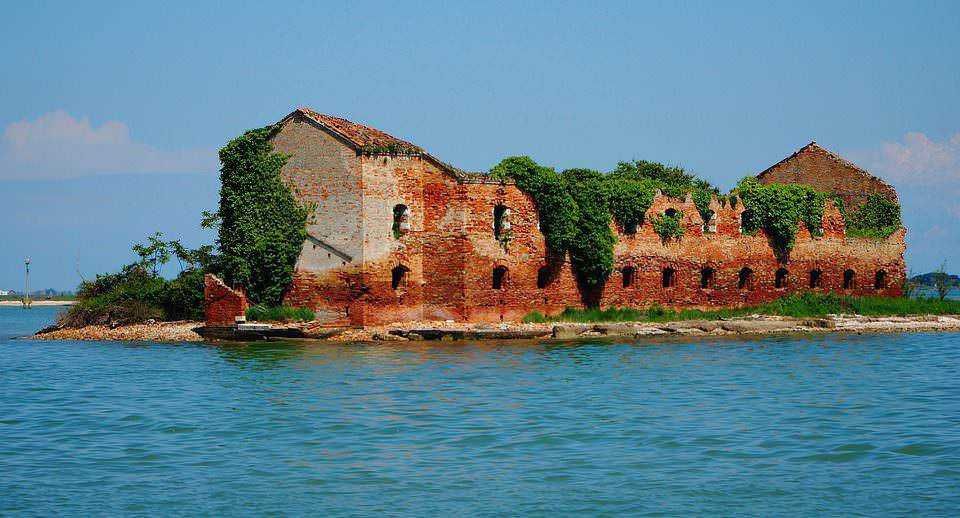 Antico edificio abbandonato su isola con vegetazione rigogliosa e acqua blu, destinazione turistica in Italia, storia e bellezza naturale, perfetto esempio di patrimonio culturale e paesaggio marino.