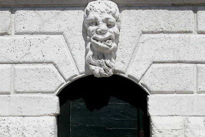 Barba e volto di pietra scolpiti sulla facciata di un edificio storico, decorazione architettonica distintiva.