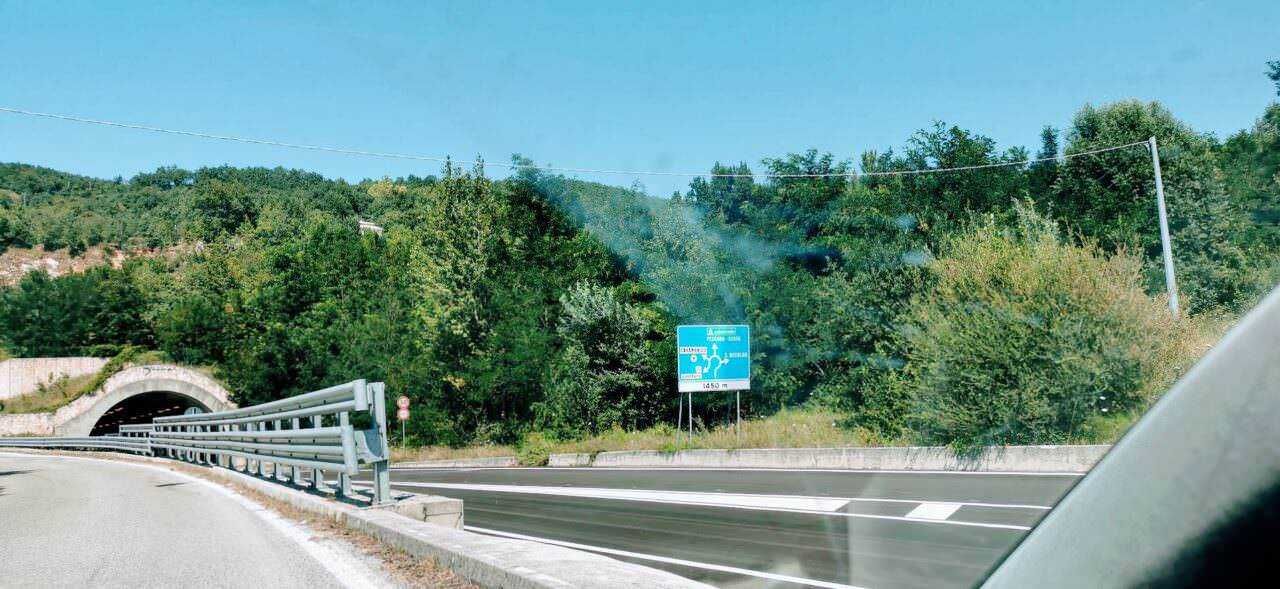 Auto strada in zona collinare con tunnel e segnale informativo, paesaggio naturale e traffico leggero, vista dinamica di un percorso stradale in Italia.